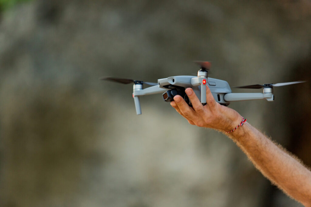 A person holding a small grey camera drone outdoors.