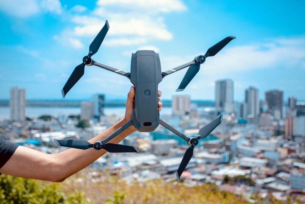 A person holding a folded-arm camera drone with a city skyline behind.