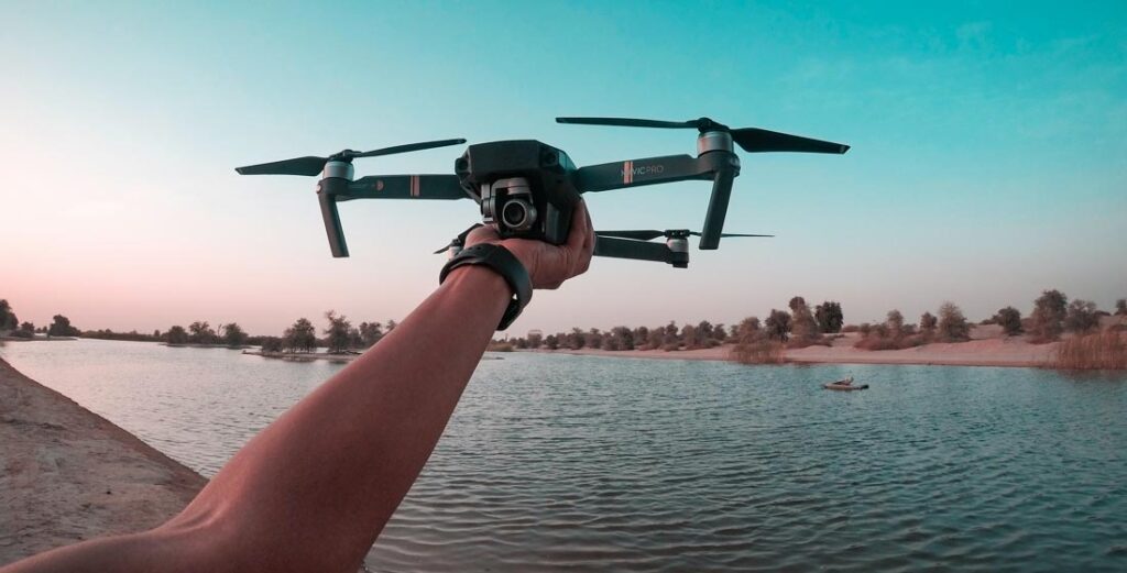 A person holding a compact drone beside water at sunset.